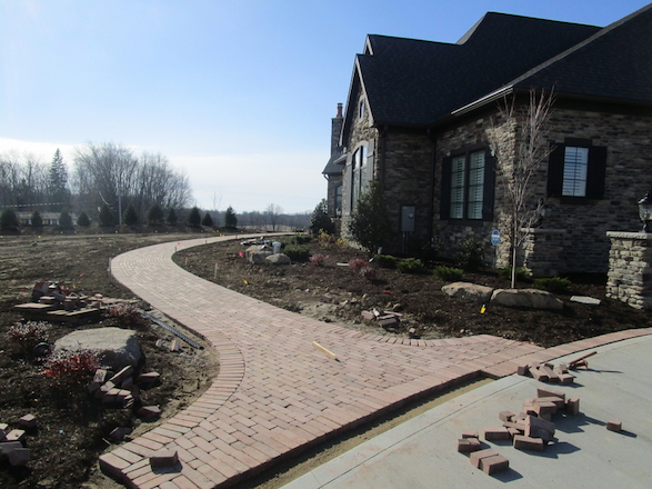 An expertly laid paver walkway curves invitingly around the grand entrance to the residence, highlighting planting beds and drawing the eye.
